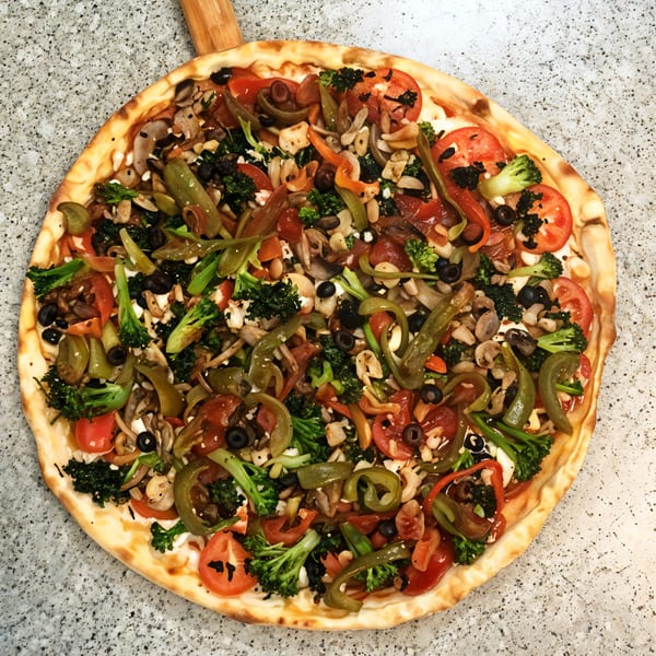 Little Anthony's vegetarian pizza with broccoli, tomatoes, peppers, olives, and mushrooms on a peel.